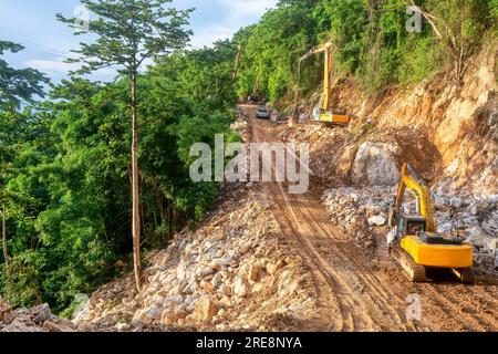 Heavy construction equipment at work building the foundation for a new road through a steep, forested area on Mindoro Island, Philippines. Stock Photo