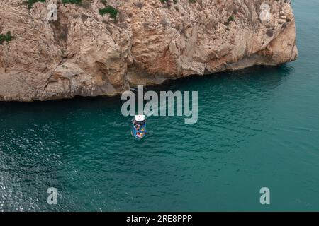 A view from above of a boat touring between two large rocky mountains in one of the beaches of the city of El Jebha, Morocco Stock Photo