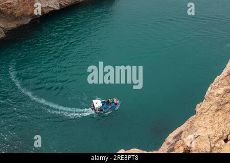 A view from above of a boat touring between two large rocky mountains in one of the beaches of the city of El Jebha, Morocco Stock Photo