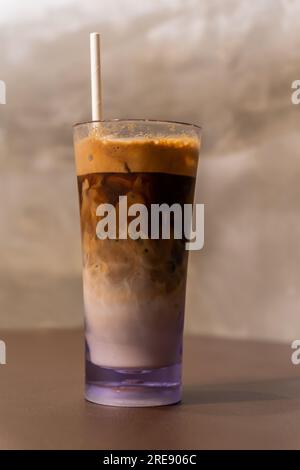 Close-up view of an iced coffee in a tall glass with cream and paper straw on a wooden table. Stock Photo