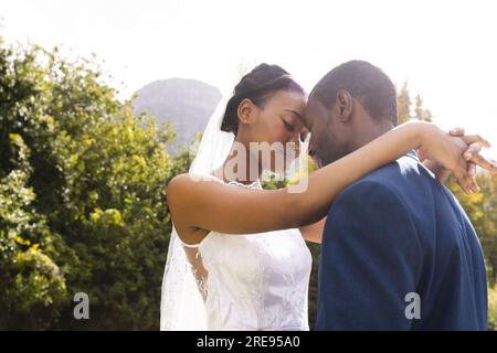 Happy african american bride and groom embracing at wedding in sunny garden Stock Photo