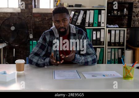 African american businessman sitting at desk, having video call and talking in office Stock Photo