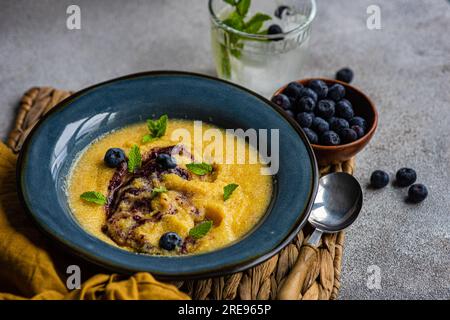 Top view of delicious traditional Italian polenta porridge topped with jam and mint leaves and served on table with bowl of fresh blueberries and glas Stock Photo