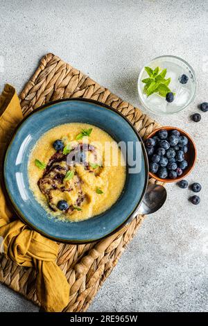 Top view of delicious traditional Italian polenta porridge topped with jam and mint leaves and served on table with bowl of fresh blueberries and glas Stock Photo