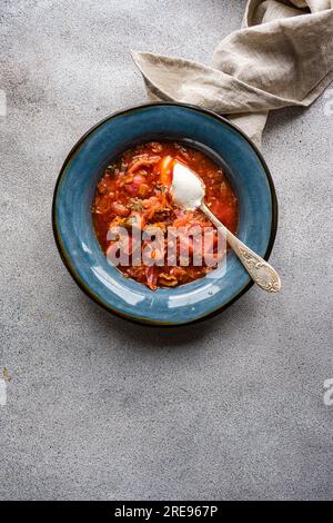Top view of bowl with traditional Ukrainian soup borscht served in blue ceramic bowl on gray surface and white sour cream sauce Stock Photo