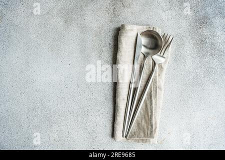 Set of cutlery placed on gray surface near rough textured background with towel napkin and dry spoon in light kitchen Stock Photo