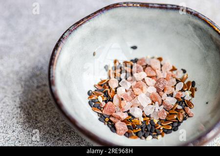 From above of bowl with salad seasoning spices mix consist of Himalayan pink salt, flax seeds, sesame seeds and black pepper on concrete background Stock Photo