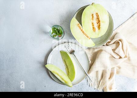 From above of green melon split in half placed in bowl and on plate with a lemonade on a concrete background Stock Photo