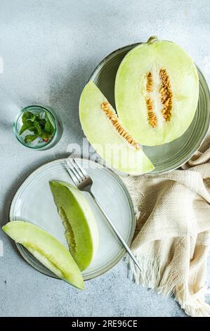 From above of green melon split in half placed in bowl and on plate with a lemonade on a concrete background Stock Photo