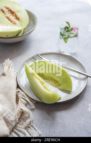From above of green melon split in half placed in bowl and on plate with a lemonade on a concrete background Stock Photo
