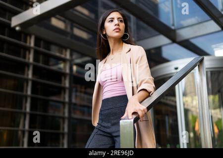 Low angle of confident female entrepreneur in formal outfit standing near entrance of office building Stock Photo