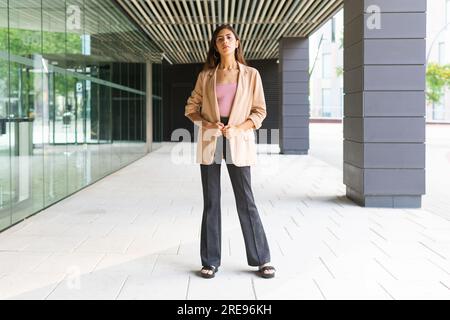 Full body of confident Hispanic female entrepreneur in formal clothes standing near office building Stock Photo