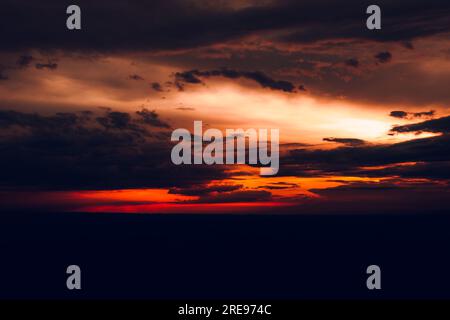 Picturesque view of orange sky with dark clouds in sunset time and blurred distant landscape in summer Stock Photo