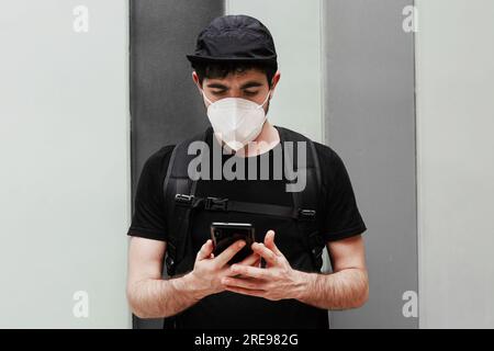 Male in black wear with rucksack using cellphone during quarantine period Stock Photo