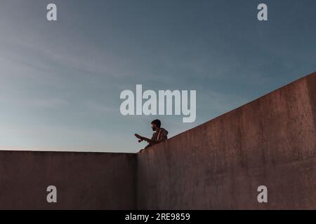 From below of young bearded male skater standing on high concrete ramp in skatepark with skateboard looking away Stock Photo