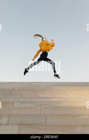 Young athletic caucasian woman wearing headphones and sport outfit, jumping on stairs outdoors Stock Photo