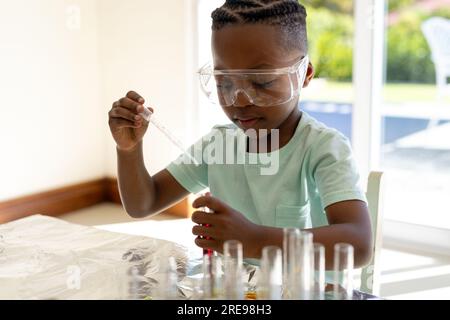 Happy african american boy doing chemistry experiments at home in sunny living room Stock Photo