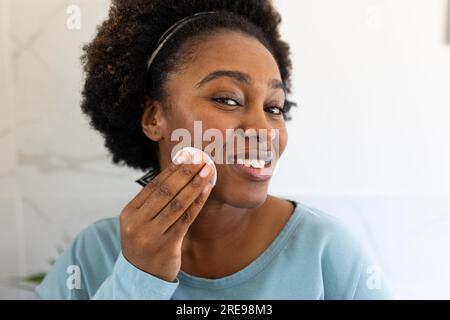 Happy plus size african american woman applying powder on face in bathroom Stock Photo