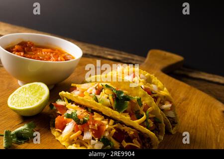 High angle view of tacos with lemon, cilantro and gravy in bowl on serving board over wooden table Stock Photo