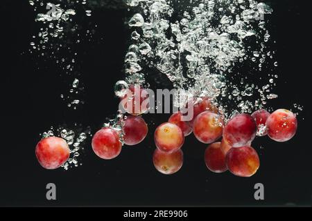 Close up of red grapes falling into water with copy space on black background Stock Photo