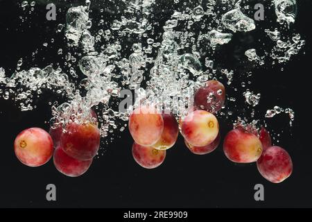 Close up of red grapes falling into water with copy space on black background Stock Photo