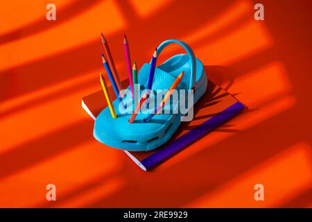 High angle of colorful pencils inserted into blue clogs placed on book against orange background during daytime Stock Photo