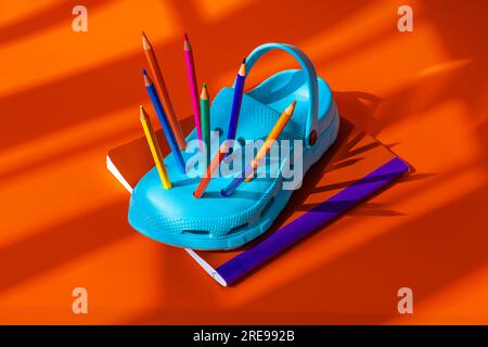 High angle of colorful pencils inserted into blue clogs placed on book against orange background during daytime Stock Photo
