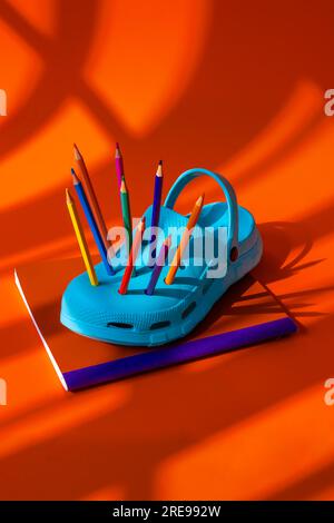 Colorful pencils inserted into blue clogs placed on book against orange background during daytime Stock Photo