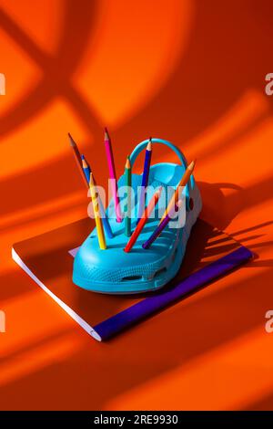 Colorful pencils inserted into blue clogs placed on book against orange background during daytime Stock Photo