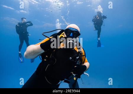 Scuba diver swimming underwater with bubbles while exploring deep clear sea during diving tour in Cancun and looking at camera against divers Stock Photo