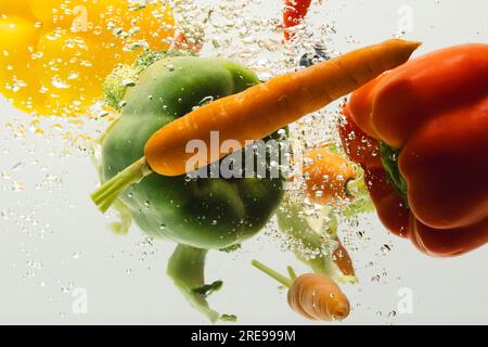 Close up of fresh vegetables falling into water with copy space on white background Stock Photo