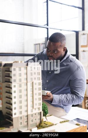 Focused casual african american businessman inspecting model of building and using calculator Stock Photo