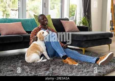 Happy african american man sitting on floor playing with his pet dog at home Stock Photo
