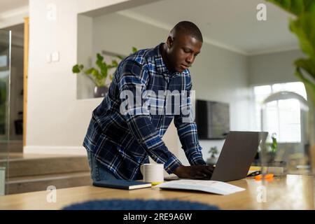 African american man standing at table using laptop at home Stock Photo