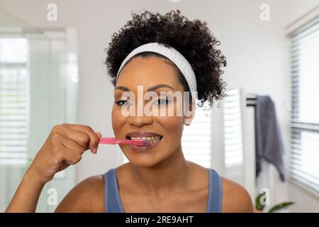 Portrait of happy biracial woman brushing teeth in bathroom Stock Photo