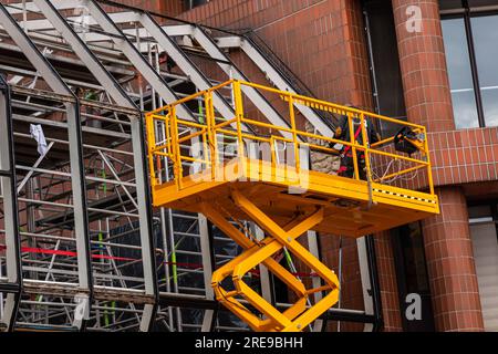 Yellow hydraulic lifting platform with bucket cabin on a telescopic lift near the building structure. Stock Photo