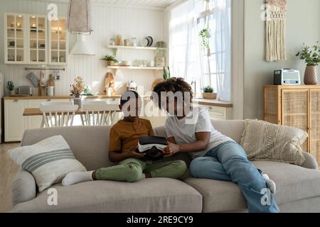 Black woman mom teaching kid son how to use VR headset for learning and education Stock Photo