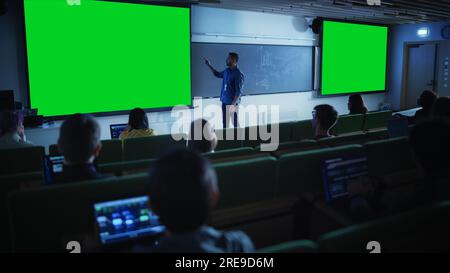 Young University Professor Explaining a Lecture, Pointing on a Green Screen Mock Up Display. Group of Diverse Multiethnic Students Stock Photo