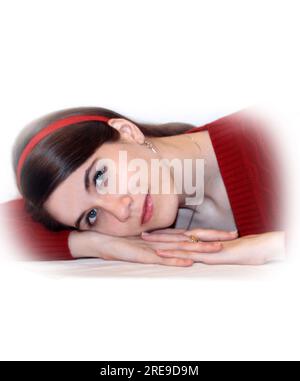 Teen wearing a red sweater, lays her head across her arms and looks dreamily at the camera.  She is in an all white room and image is isolated. Stock Photo