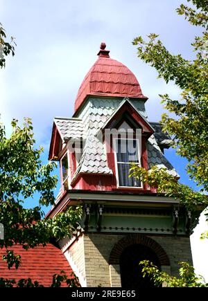 Beautiful Queen Ann Victorian home has a square tower topped with a four sided dome with four dormers.  Wooden shingles are faded pastel green. Stock Photo