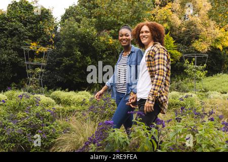 Portrait of happy diverse couple holding hands, walking in garden, copy space Stock Photo