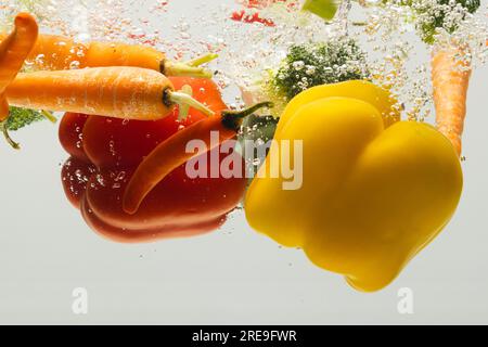 Close up of fresh vegetables falling into water with copy space on white background Stock Photo