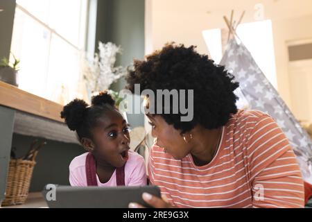 Happy african american mother and daughter playing in tent, using tablet at home Stock Photo