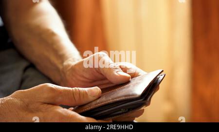 An elderly man's hands, covered with knotted veins, search for coins in his wallet Stock Photo