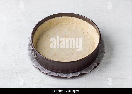 Cheesecake making, metal detachable baking dish with shortcrust pastry for cheesecake or other pie. Step by step, cooking stage, home baking, light gr Stock Photo