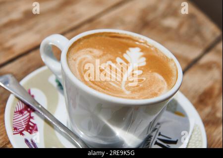 Coffee with milk in white cup with floral drawing on the surface Stock Photo