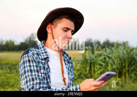 Farmer using phone. a dedicated farmer stands, attentively examining the crops that have emerged after sowing Stock Photo