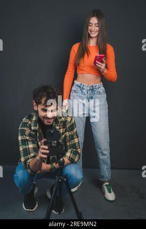 Young smiling man and woman blogger influencers shooting themselves on smartphone isolated over black background. Making vlog. Vlog concept Stock Photo