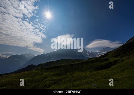 Starburst sun and lenticular clouds over the Eiger, Jungfrau and Moensch mountains, seen from Mannlichen above Wengen, Bernese Oberland, Switzerland Stock Photo