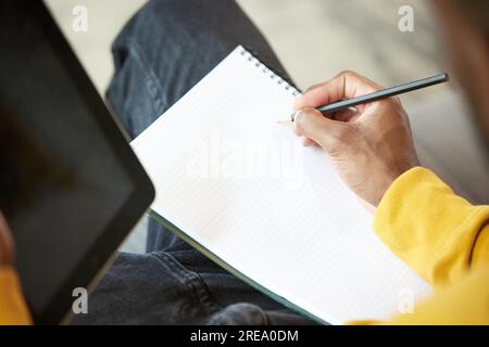 Close-up image of male hand holding pencil, making notes on notebook, listening to video lessons, online meeting Stock Photo